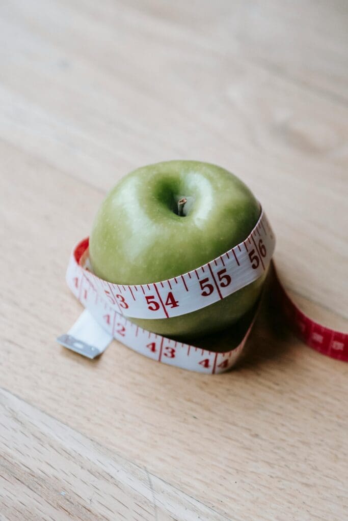 Green apple wrapped with a measuring tape on a wooden table, representing weight management through GLP-1 concierge services.