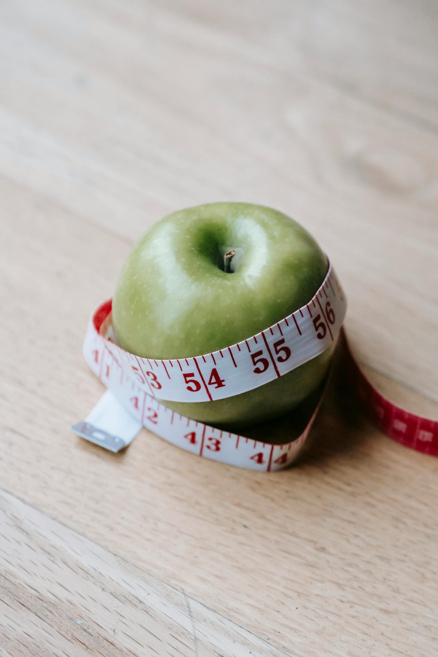 Green apple wrapped with a measuring tape on a wooden table, representing weight management through GLP-1 concierge services.